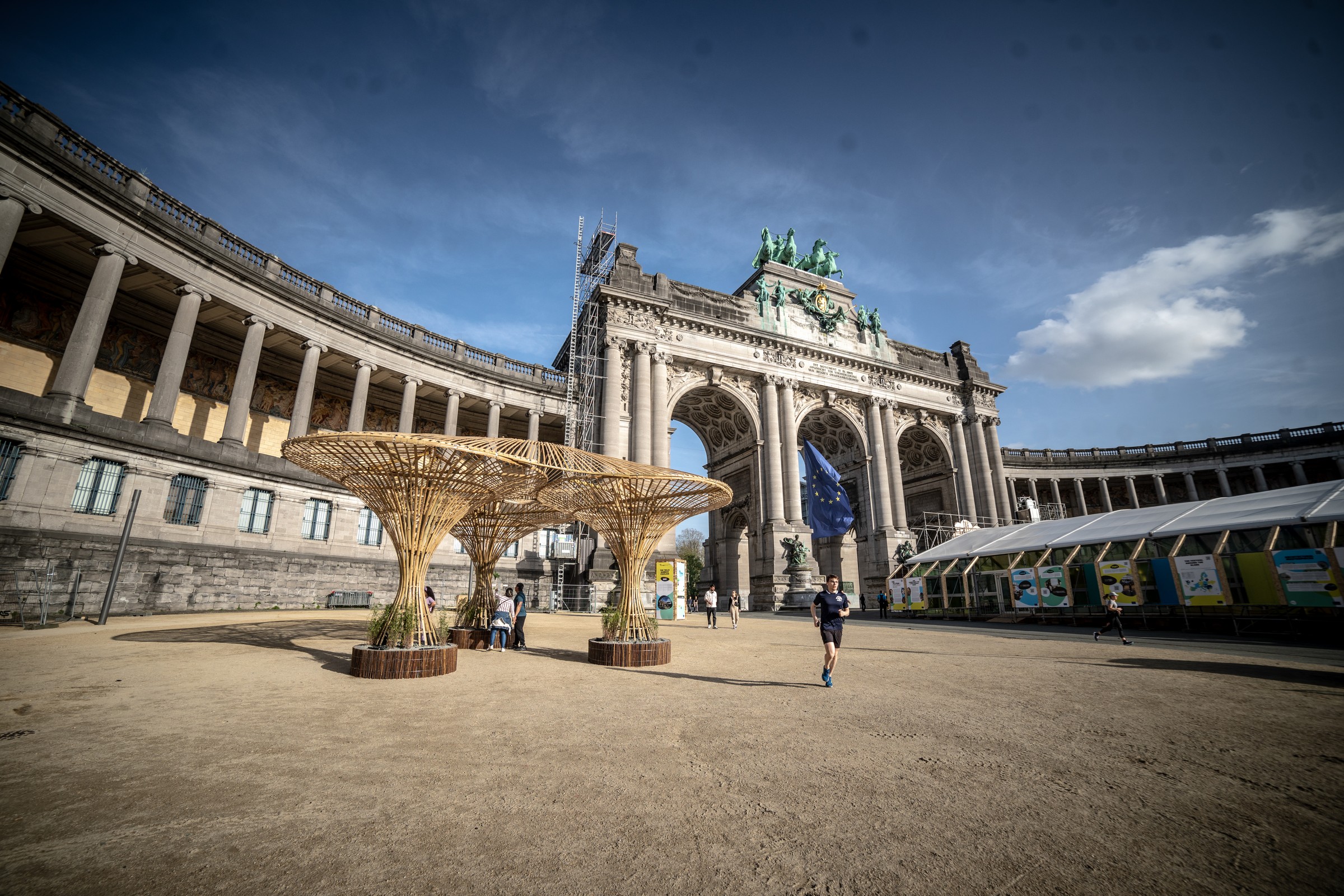 Bamboo pavilion with three flared column supports in front of the Cinquantenaire triumphal arch, Brussels, daylight
