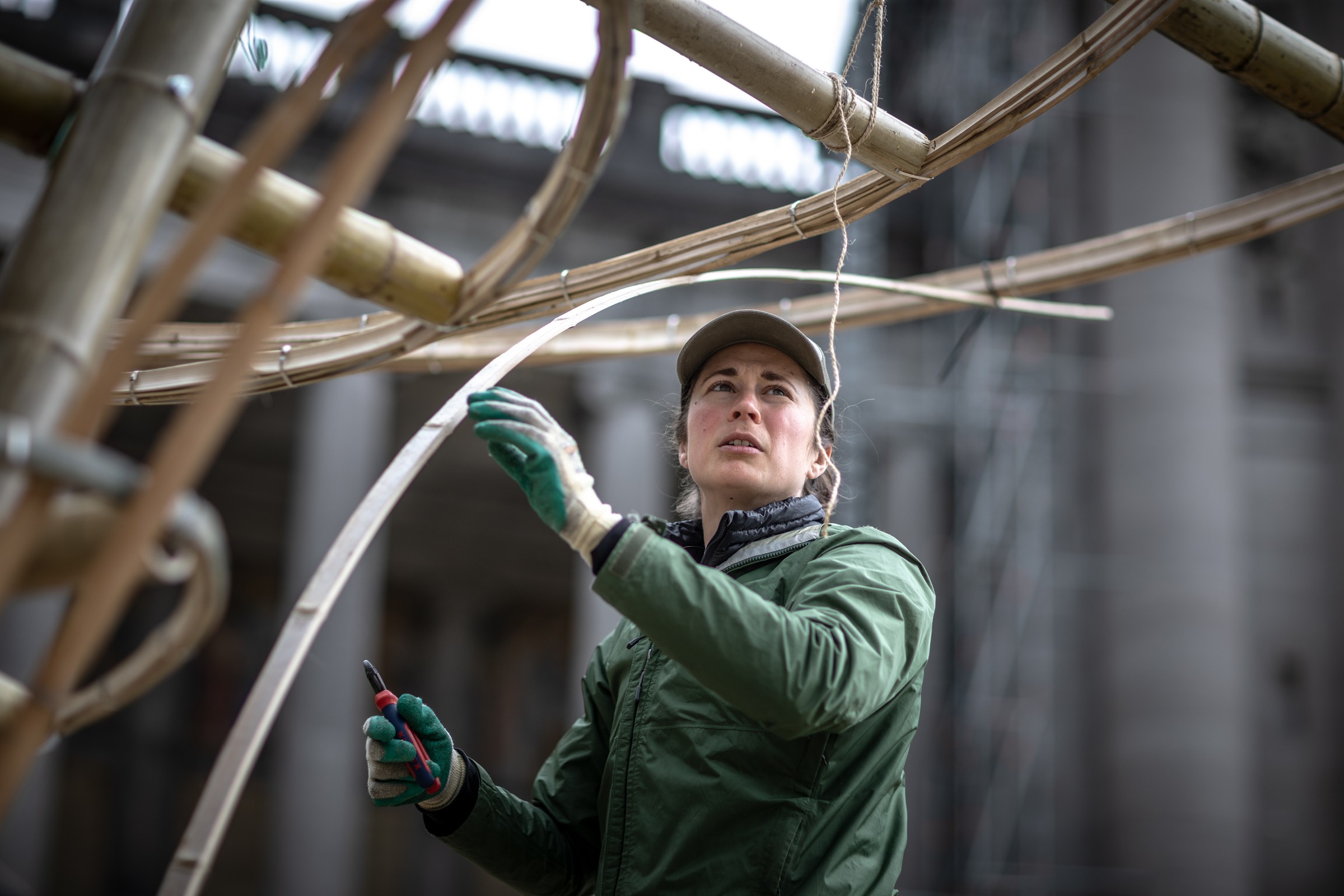 Practitioner in green jacket adjusting a curved bamboo element during pavilion construction