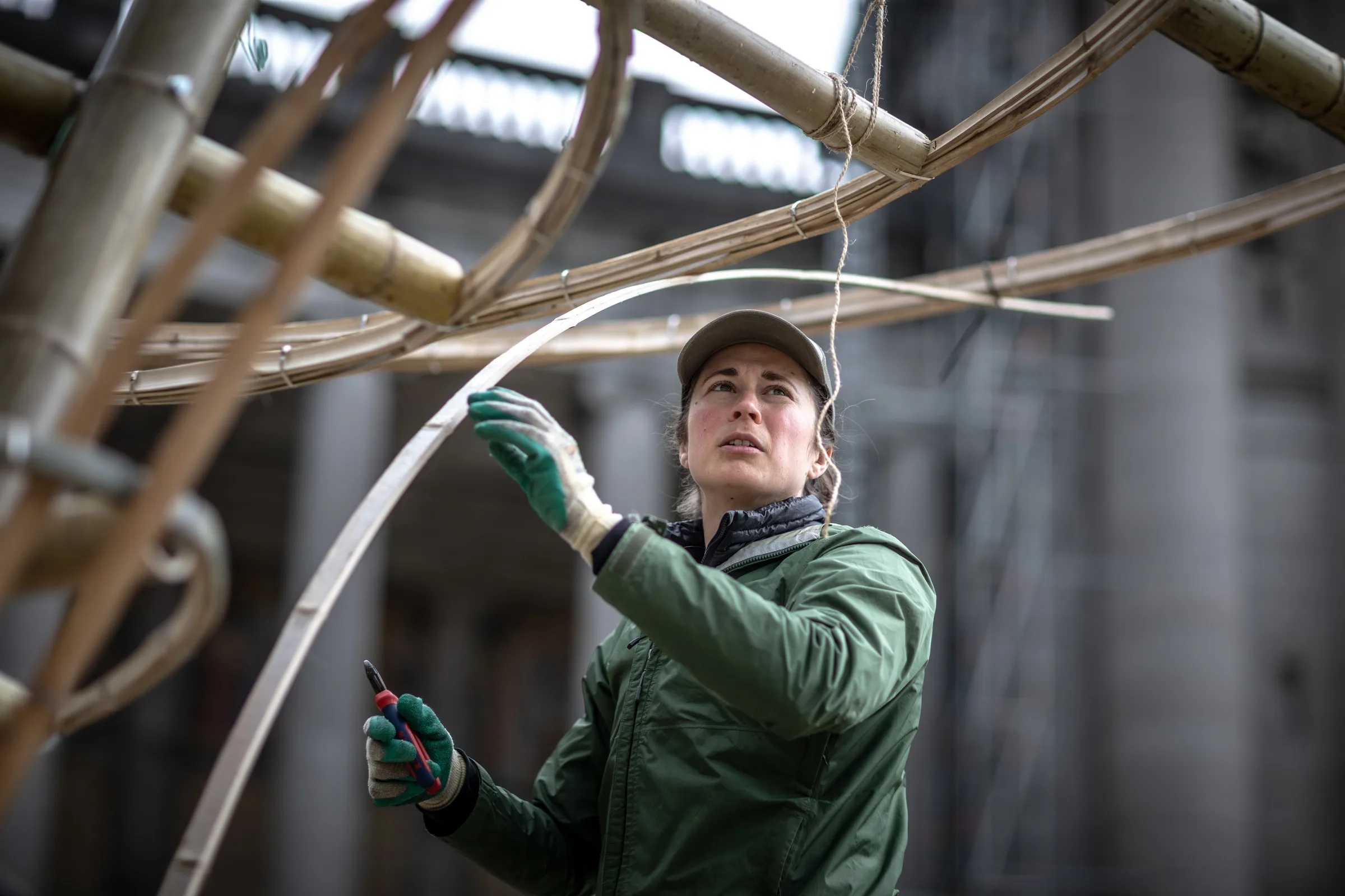 Practitioner in green jacket adjusting a curved bamboo element during pavilion construction