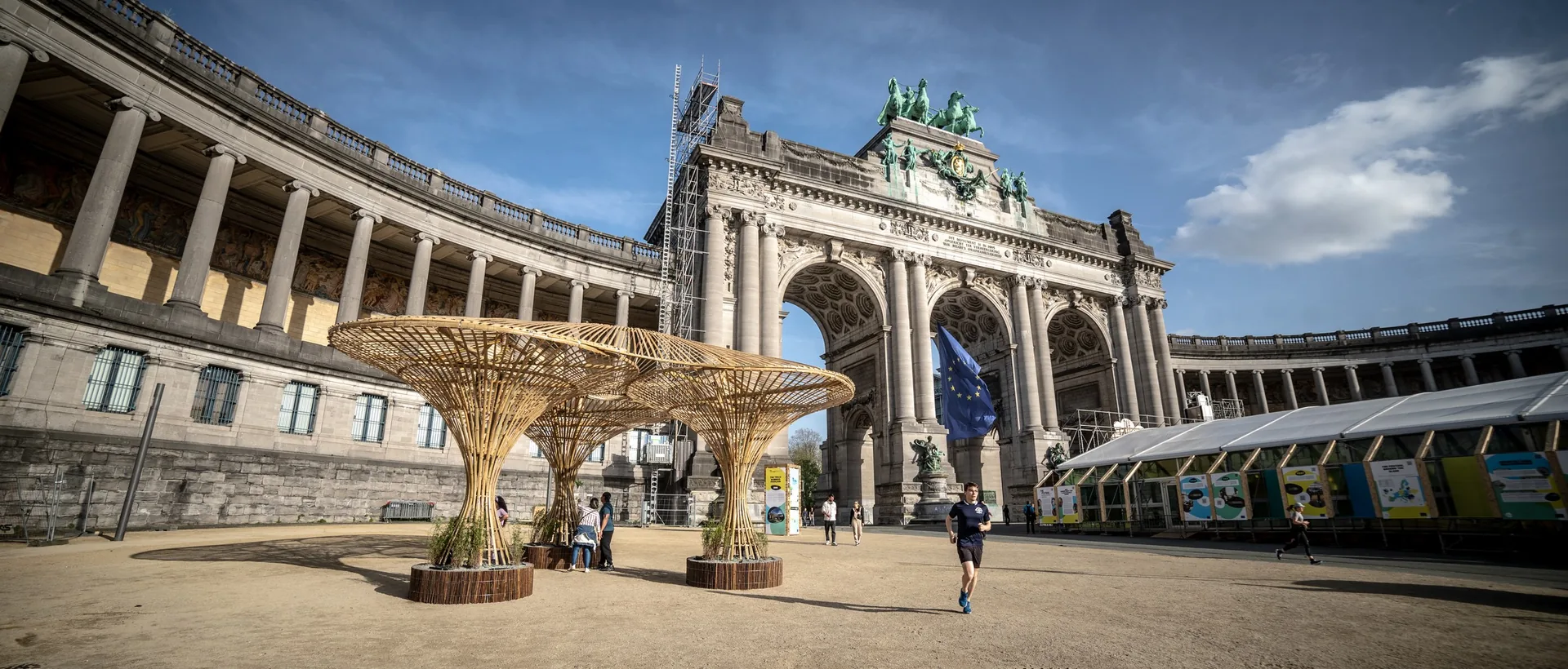 Bamboo pavilion with three flared column supports in front of the Cinquantenaire triumphal arch, Brussels, daylight